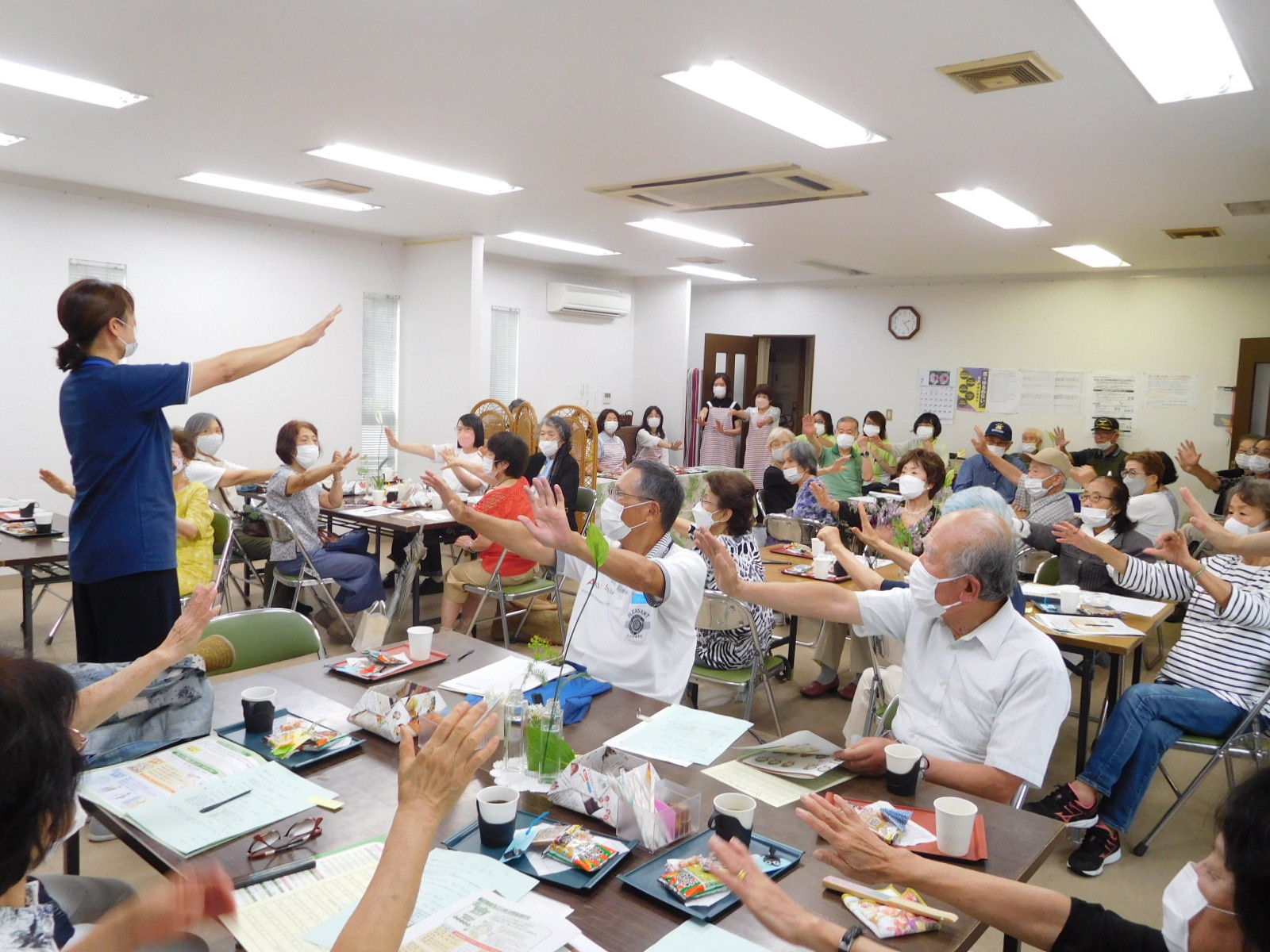 ポピュレーションアプローチの様子、高齢者複数名が資料を見ながら講師をまねて腕を伸ばしている