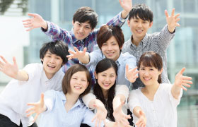 大学生男女複数名がこちらに手を伸ばして微笑んでいる