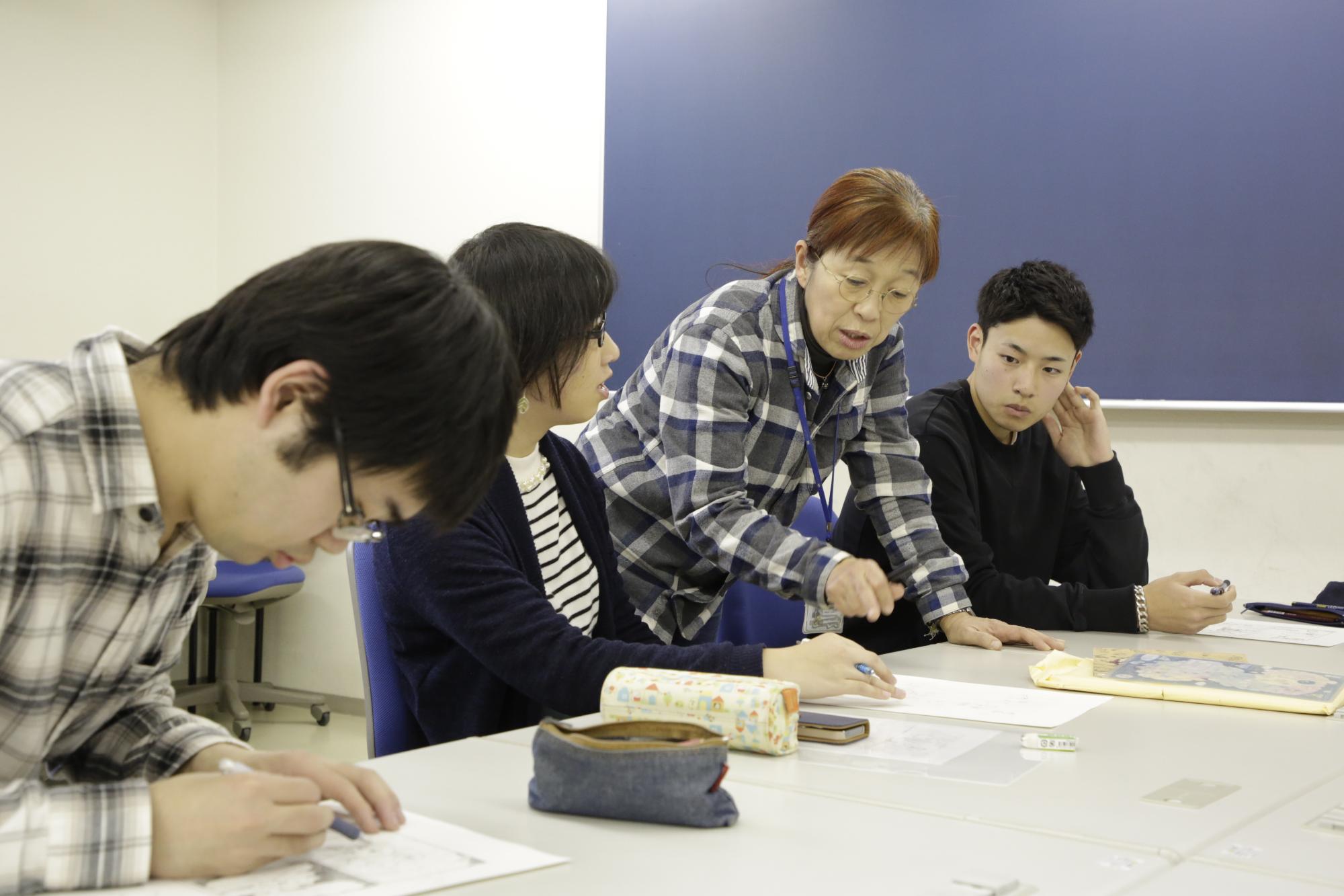 講義中の様子を写した写真。学生の手元にはマンガの原稿があり、講師から直接指導を受けている様子が写されている。