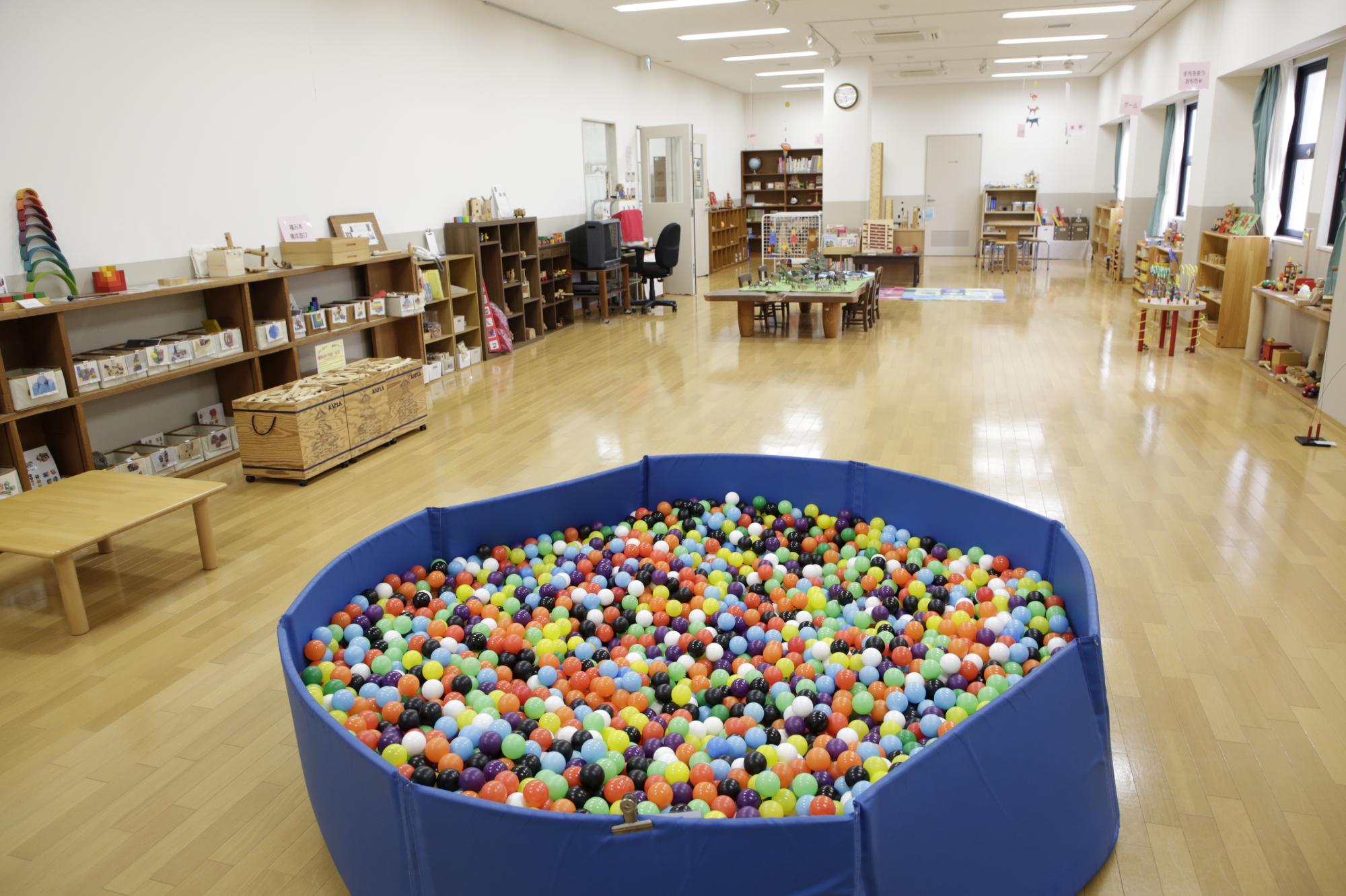 子供センター内部の様子を写した写真。手前にボールプールが置かれており、奥には子供用の机やおもちゃが置かれている。